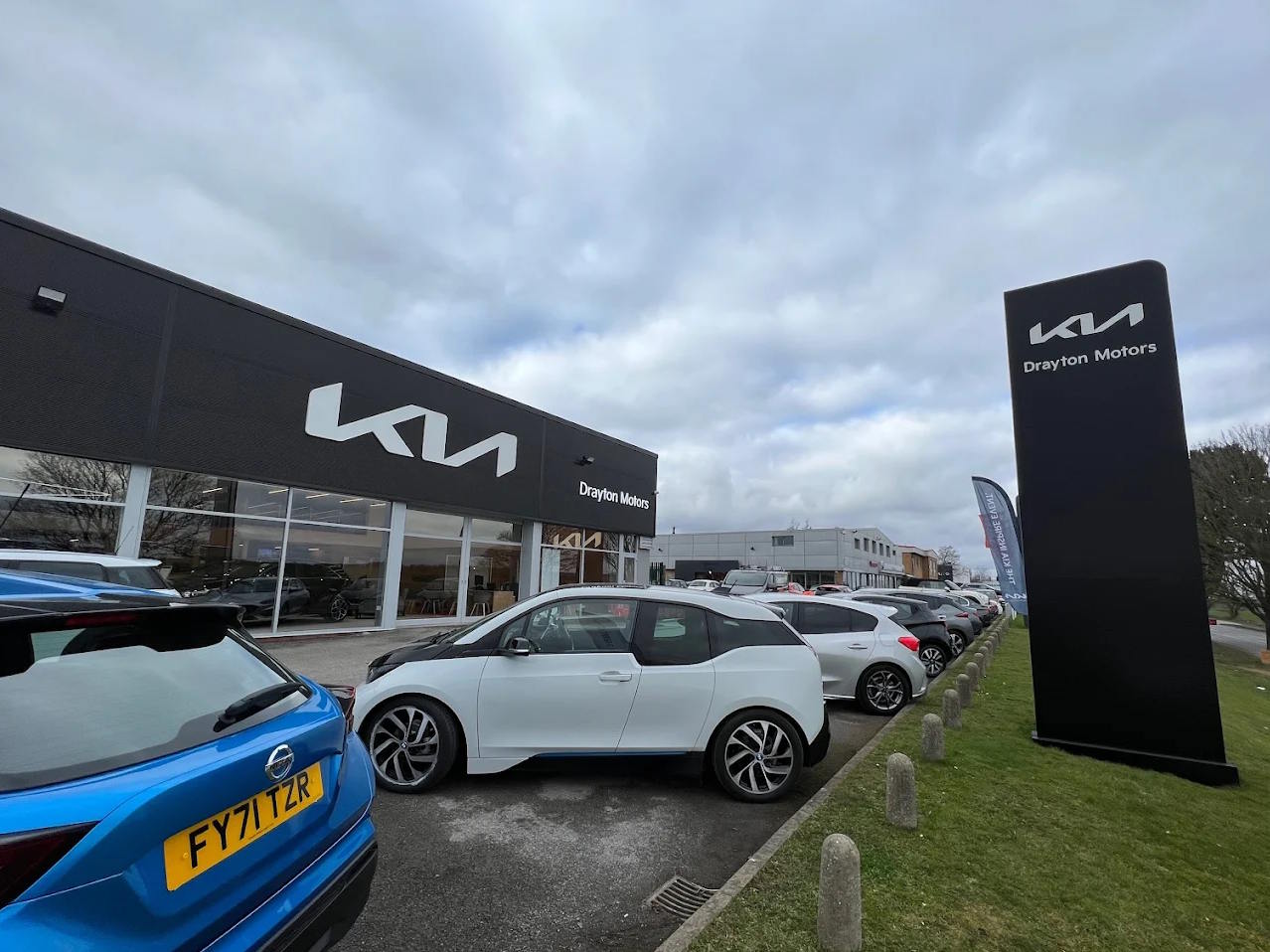 Exterior view of Drayton Motors Kia Grantham dealership, featuring a blue Nissan on the forecourt with modern showroom and branded signage