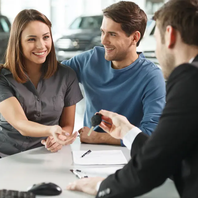 Three people with the the car dealer giving car keys to a woman 