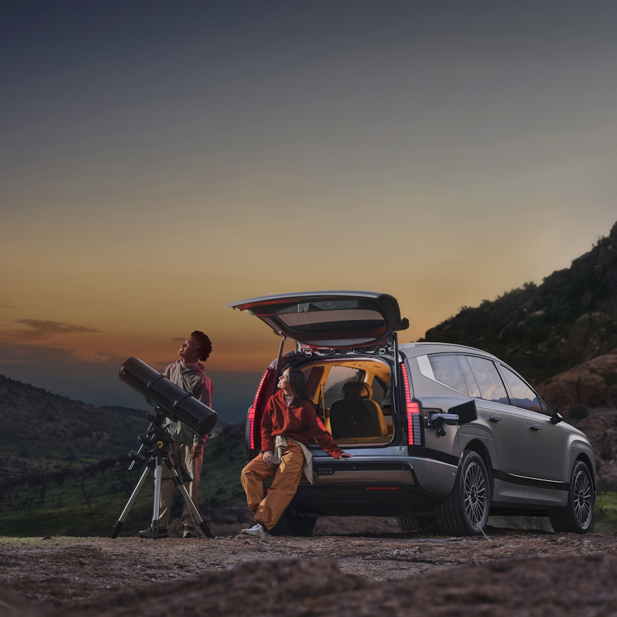 people  sat in the boot of a Ioniq 9 looking through binoculars 