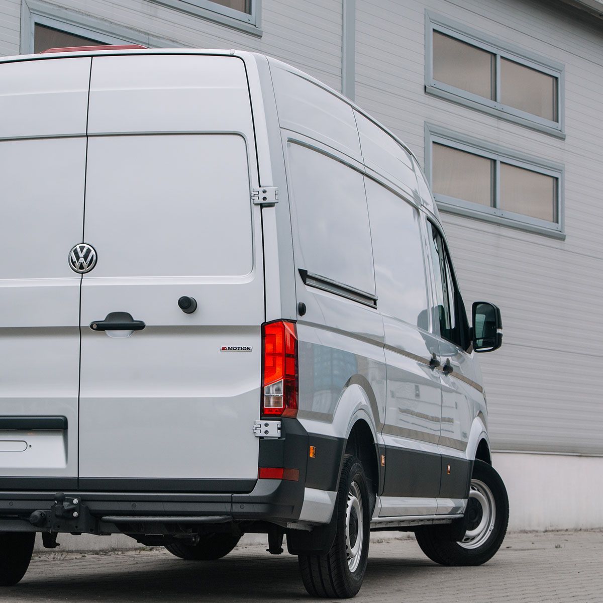 White Volkswagen Crafter van parked outside a warehouse, rear three-quarter view.