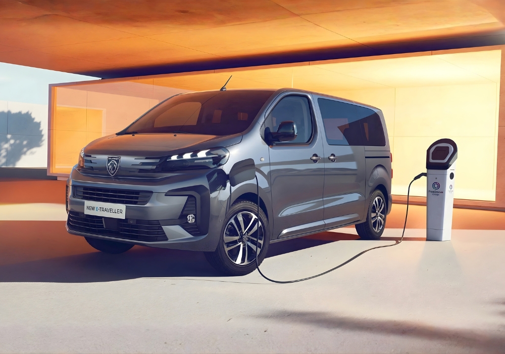 Peugeot E-Traveller in grey connected to an electric charging station in a modern outdoor setting.