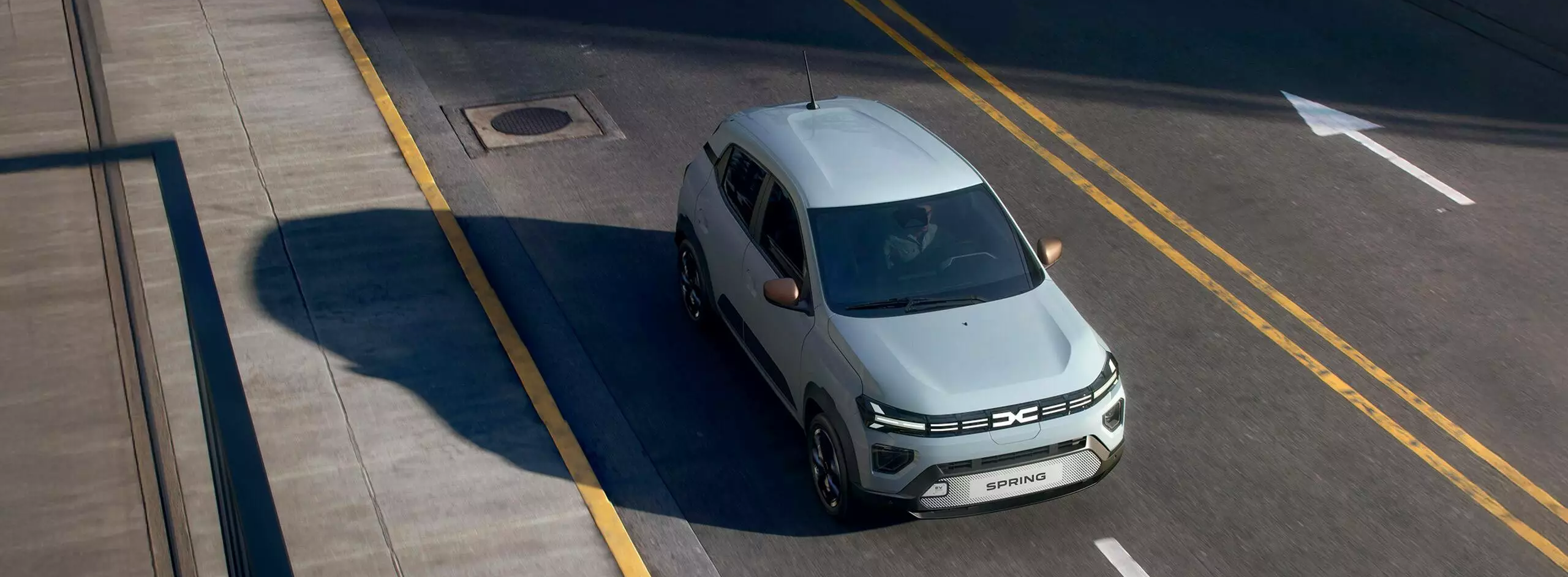 Dacia Spring driving along a city street from an overhead angle, showing compact design and urban setting.