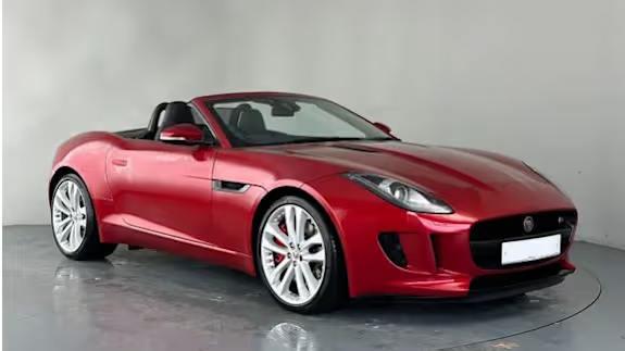 Red Jaguar F‑Type convertible sports car, roof down, parked in a studio with a plain grey background.