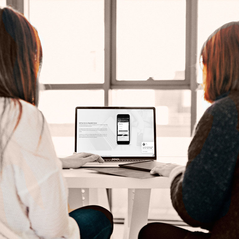 Two people viewing a website on a laptop while seated at a table.
