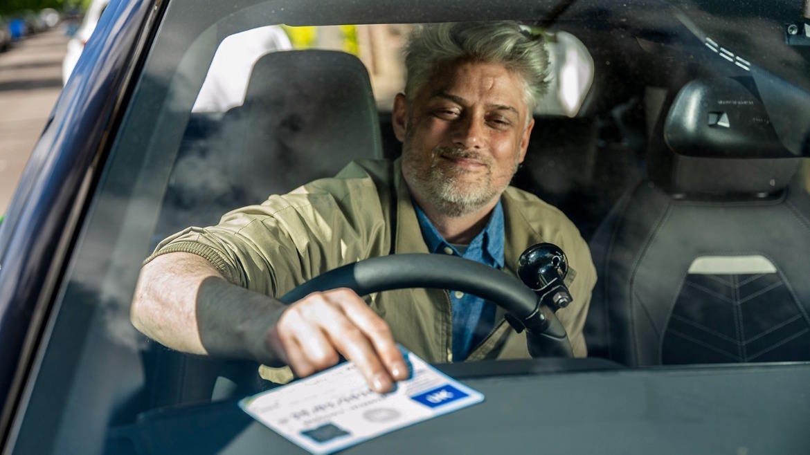 Driver placing a disabled parking badge on the dashboard of a modern vehicle, viewed through the windscreen with contemporary interior visible behind
