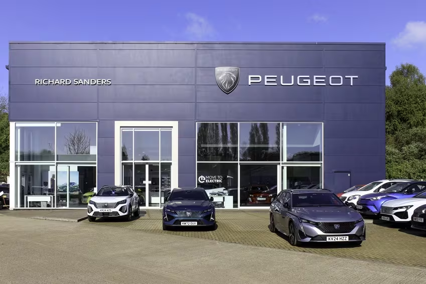 Exterior view of Peugeot dealership with multiple Peugeot models displayed outside and showroom signage visible.