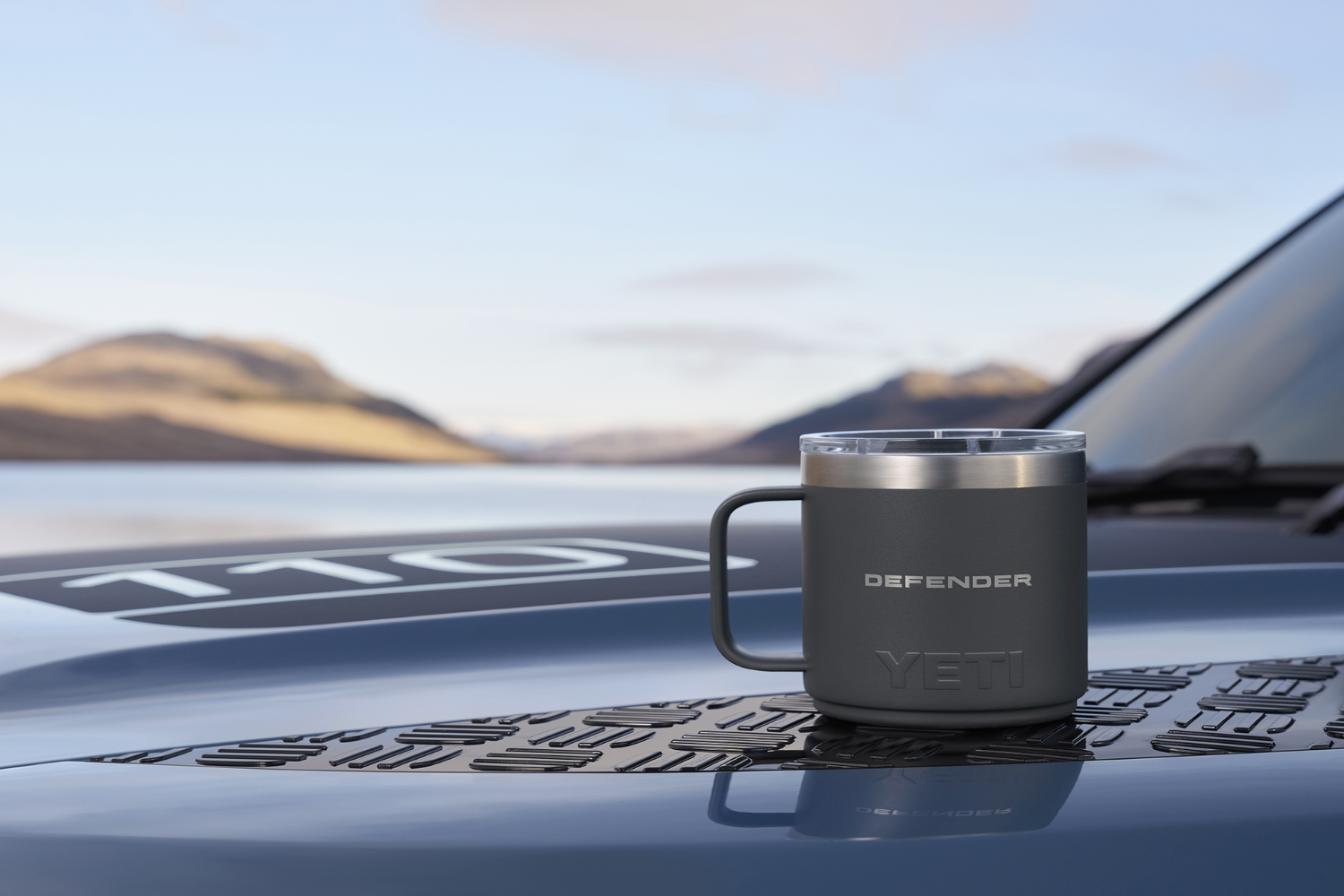 Defender branded YETI mug placed on bonnet overlooking scenic landscape.