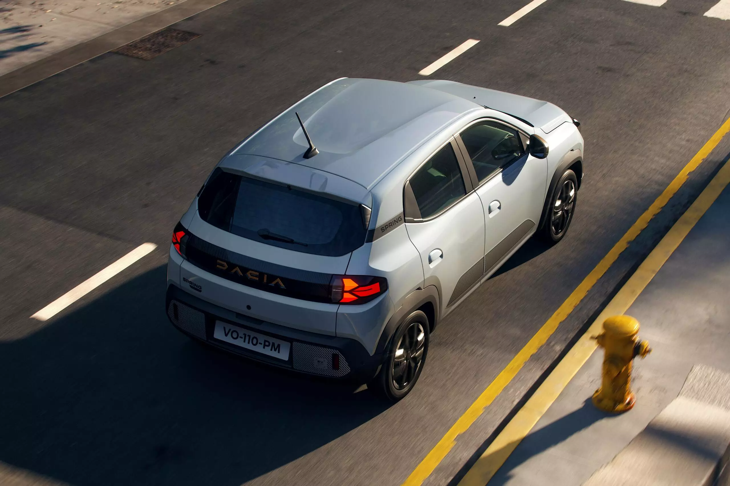 Dacia Spring driving through a city road from the rear, highlighting compact size and modern rear design.