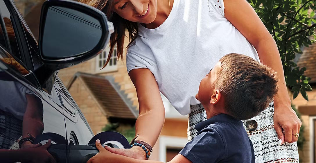 Woman and child connecting a charging cable to an electric car at home.