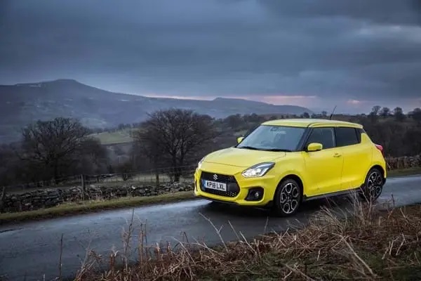 Yellow Suzuki Swift Sport driving along road at night