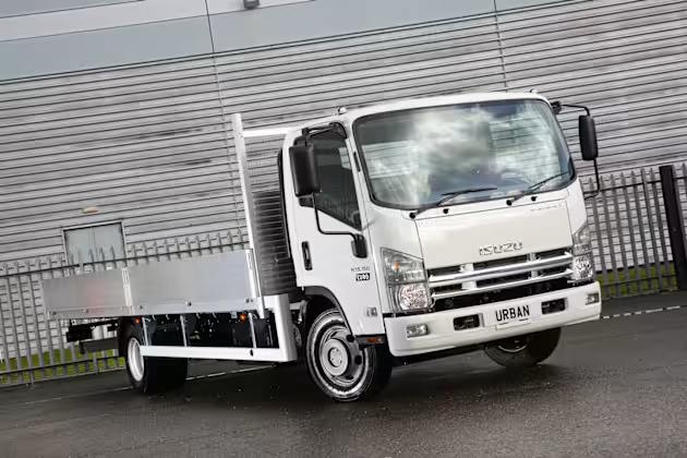Front three-quarter view of Isuzu Urban flatbed truck highlighting cab design and load platform.
