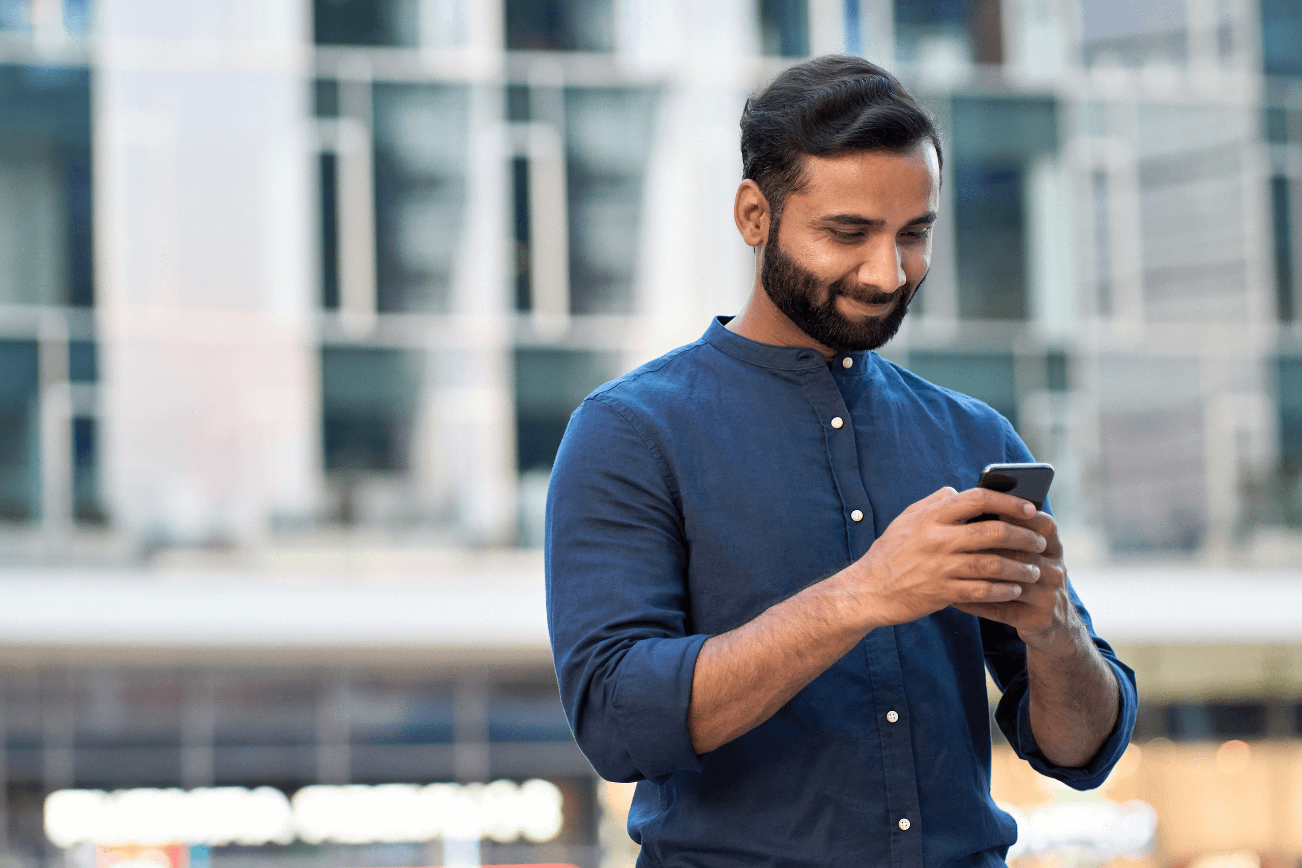Man in navy shirt, holding his phone with both hands and smiling.