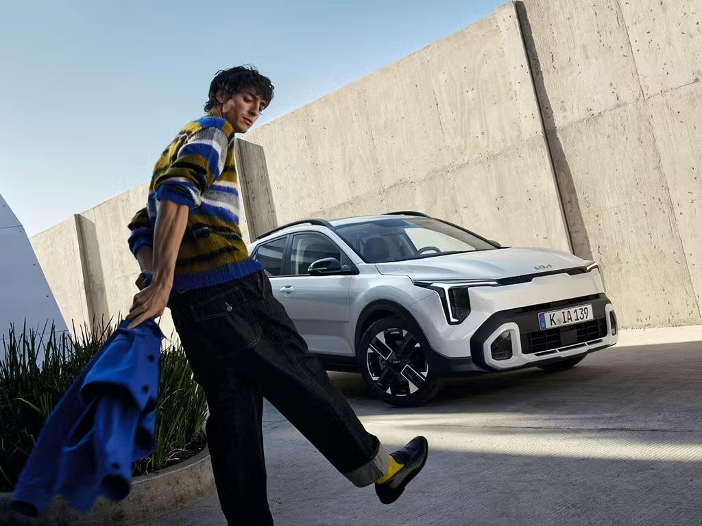 Front three-quarter view of the white Kia Stonic compact SUV, featuring its distinctive tiger-nose grille, sharp LED headlight signature and bold two-tone alloy wheels in an urban concrete setting.