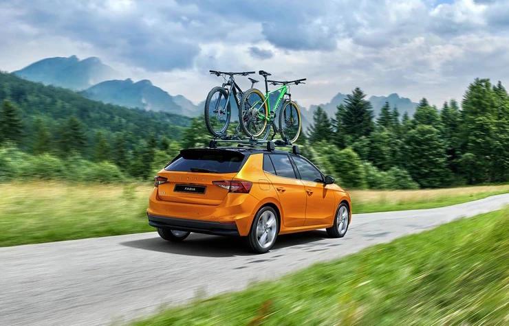 Orange Skoda Fabia driving on a rural road with two bicycles mounted on the roof.