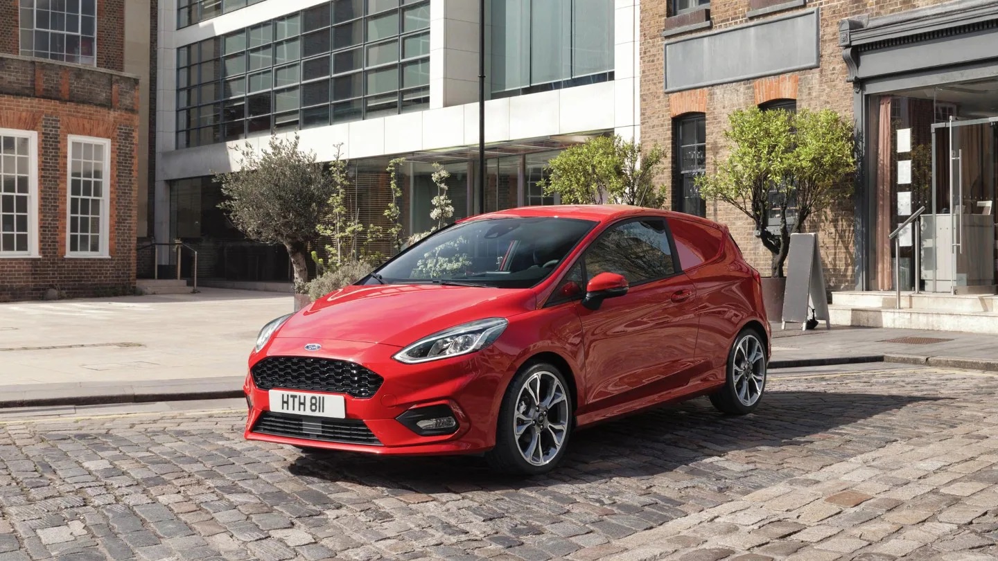 Red Ford Fiesta Van parked in front of buildings
