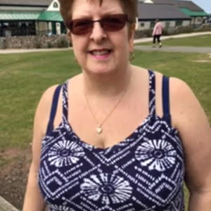 Person standing outdoors on a grassy area wearing sunglasses and a patterned summer top.