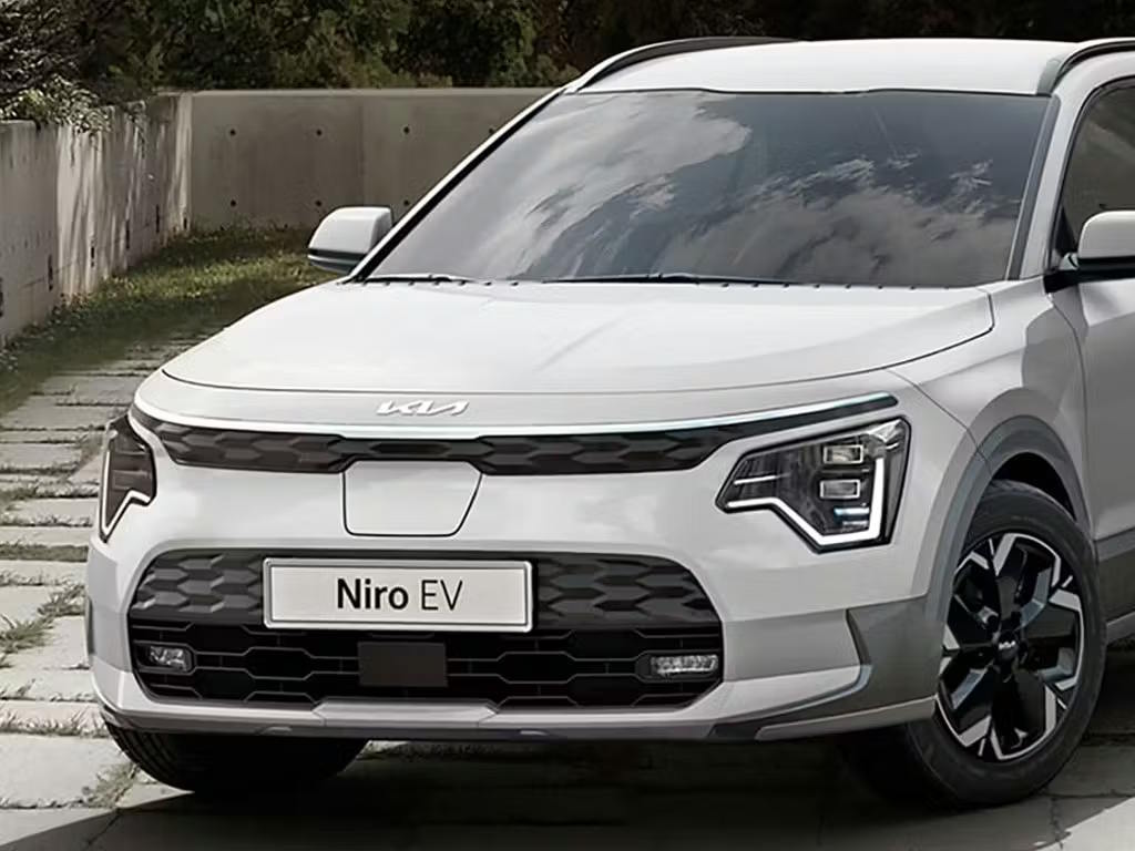 Front three-quarter view of the Kia Niro EV in white, featuring distinctive boomerang-shaped LED daytime running lights, closed grille design and contrasting black alloy wheels.