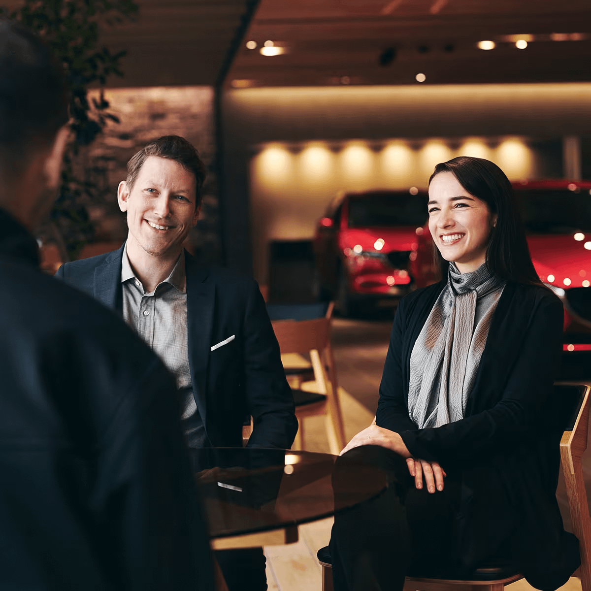 man and woman smiling at someone in a car dealership
