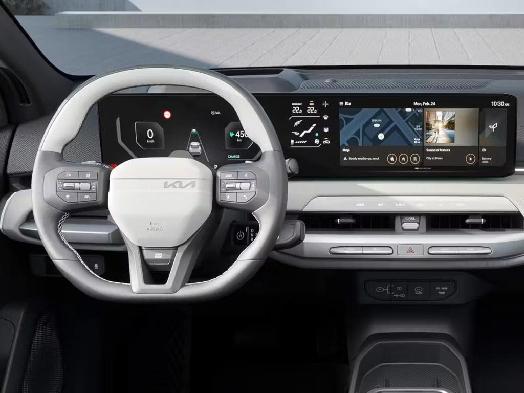 Interior view of the Kia EV4, featuring a two-spoke steering wheel, curved dual-screen dashboard display, light grey trim and minimalist centre console design.