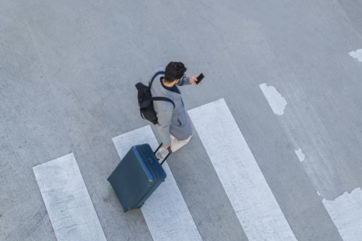 man pulling suitcase crossing the road and on his phone