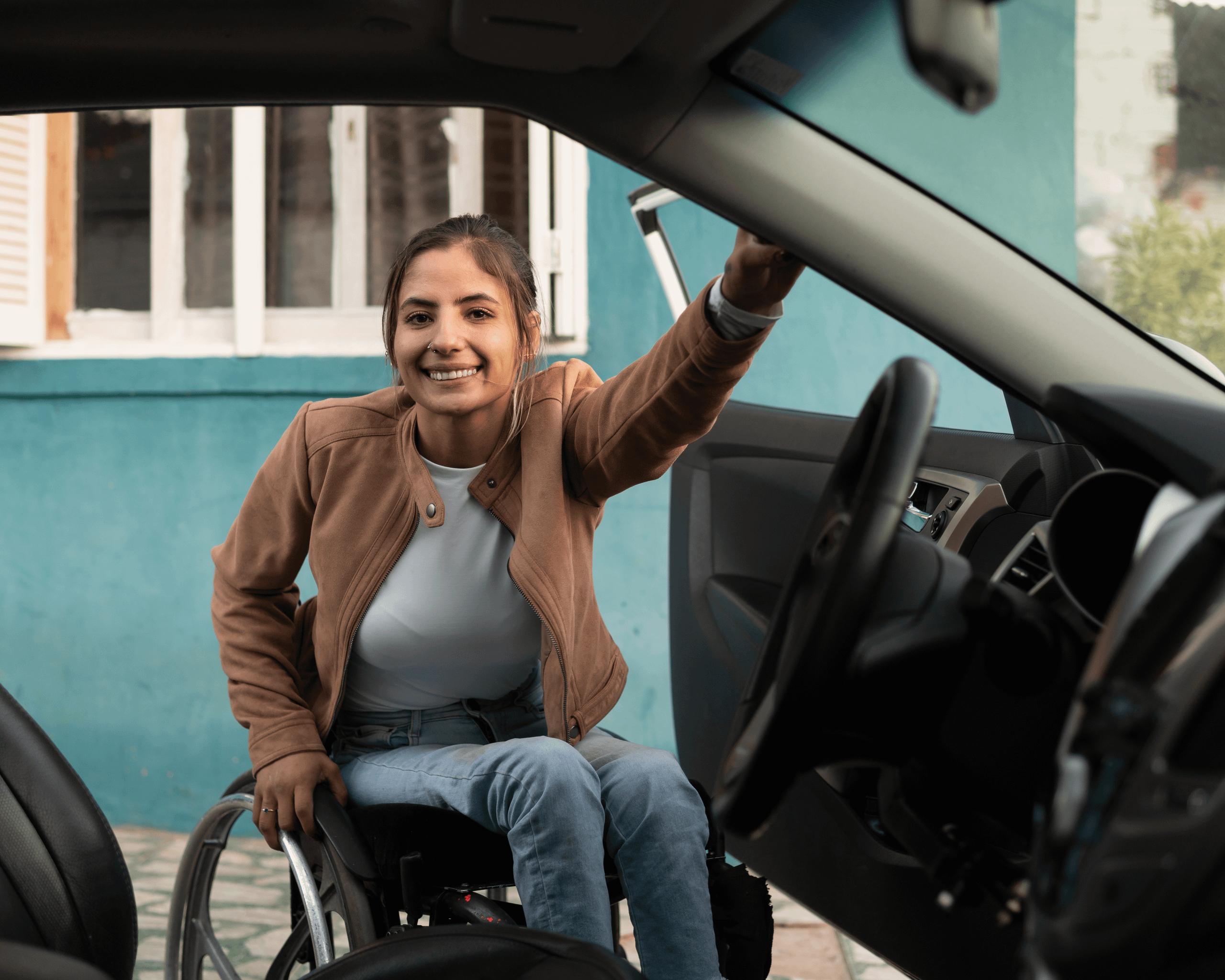 Smiling wheelchair user opening a car door and preparing to get into the driver’s seat outside a house.