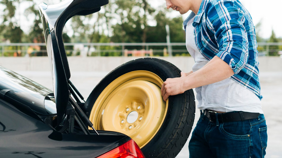 spare tyre being pulled from the rear of the car to replace a flat tyre