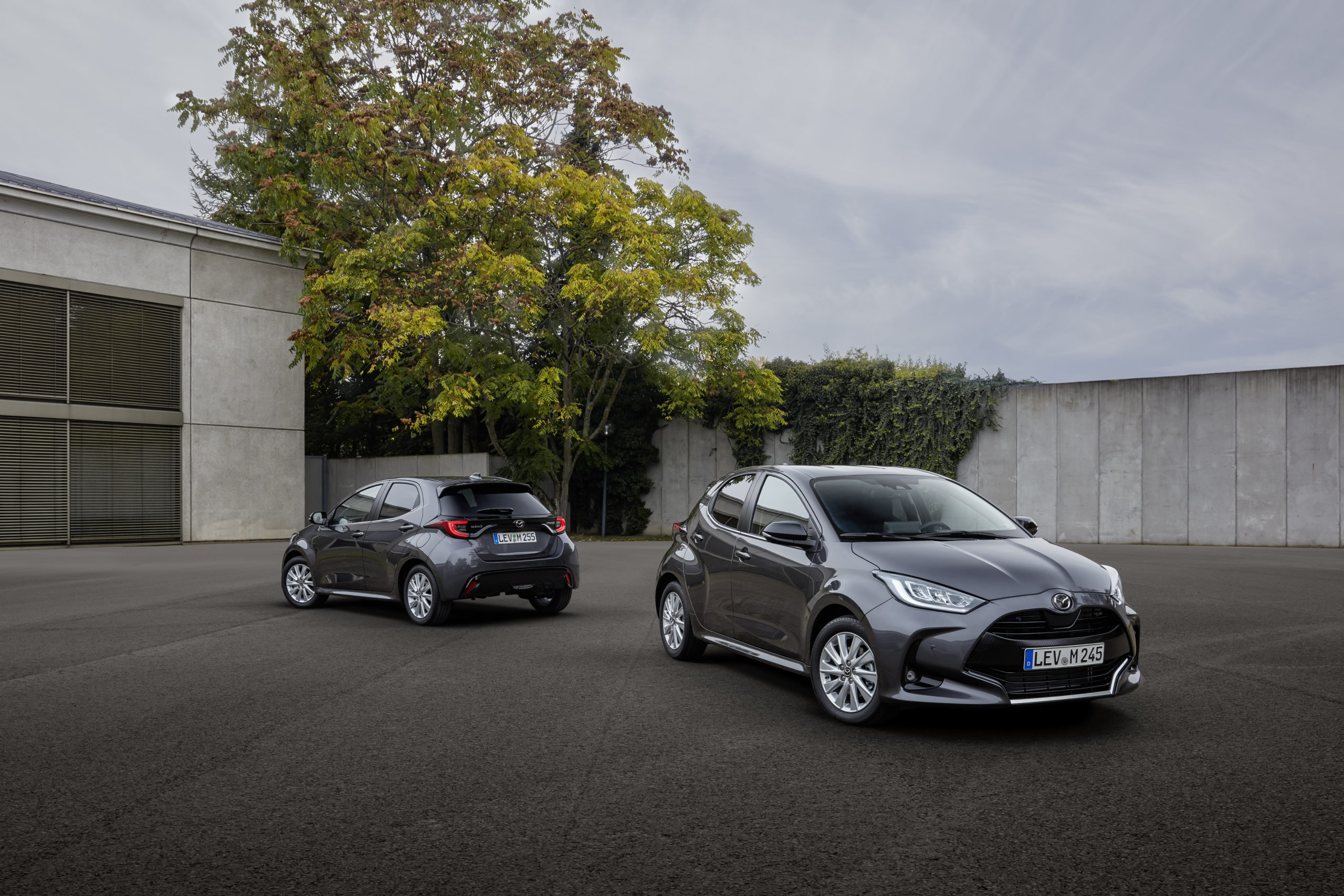 A pair of grey Mazda 2 Hybrids parked in an open urban car park.