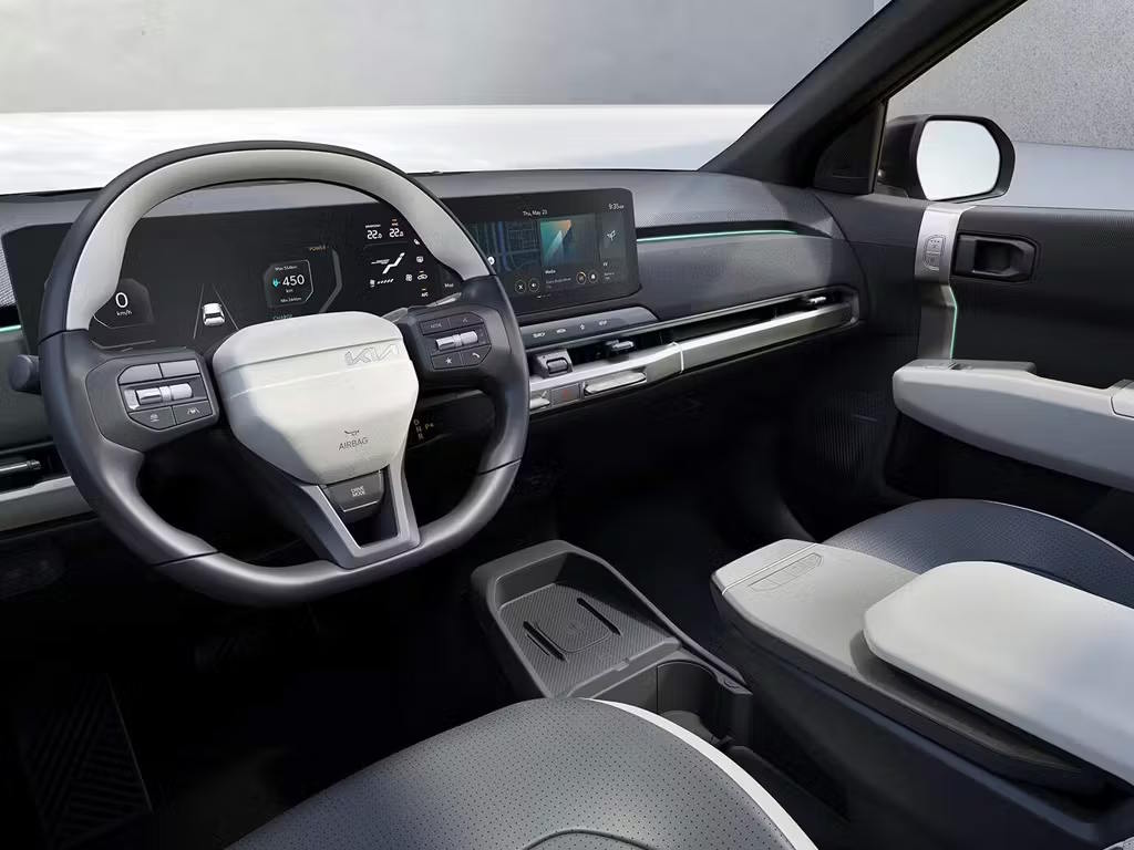 Interior view of the Kia EV3 showcasing the modern dashboard with dual widescreen displays, two-spoke steering wheel and sustainable textile seat upholstery in grey tones.