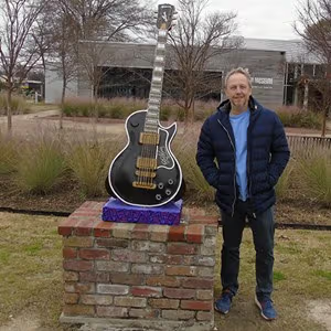 Outdoor portrait of a person next to a guitar monument in a landscaped setting.
