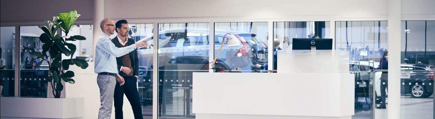 Business professionals inside a dealership talking and pointing at something.