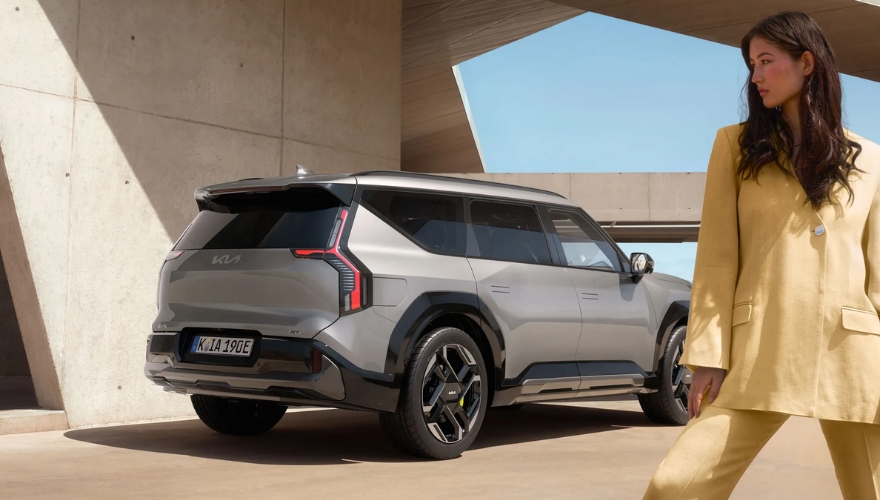 Side view of a grey Kia EV9 GT stationary outside a contemporary building.