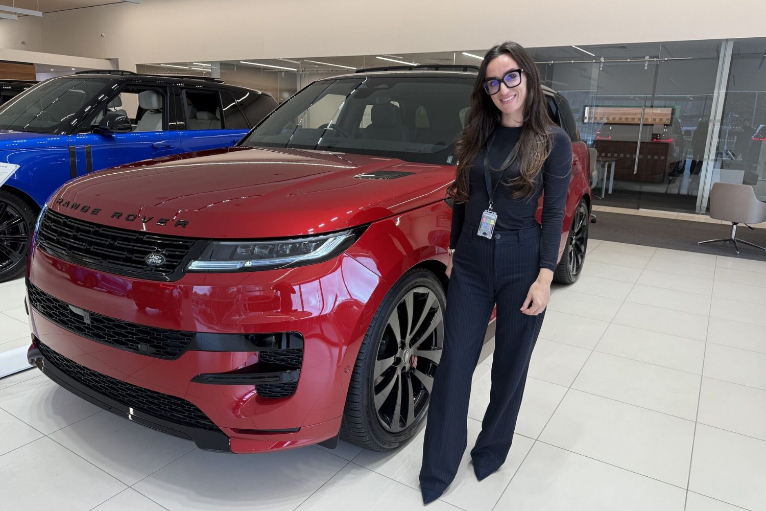 A woman standing in a car showroom next to a red Range Rover Sport, with other Range Rover vehicles visible in the background.
