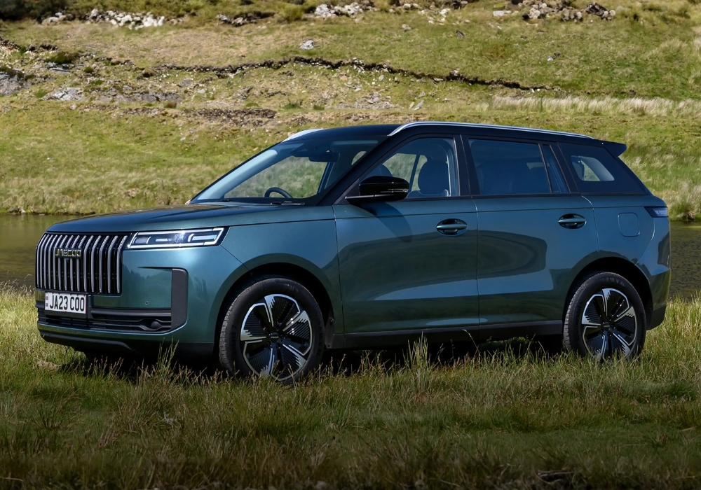 Green Jaecoo 5 SUV parked on grassy terrain beside a lake, shown in full side profile with hills behind.