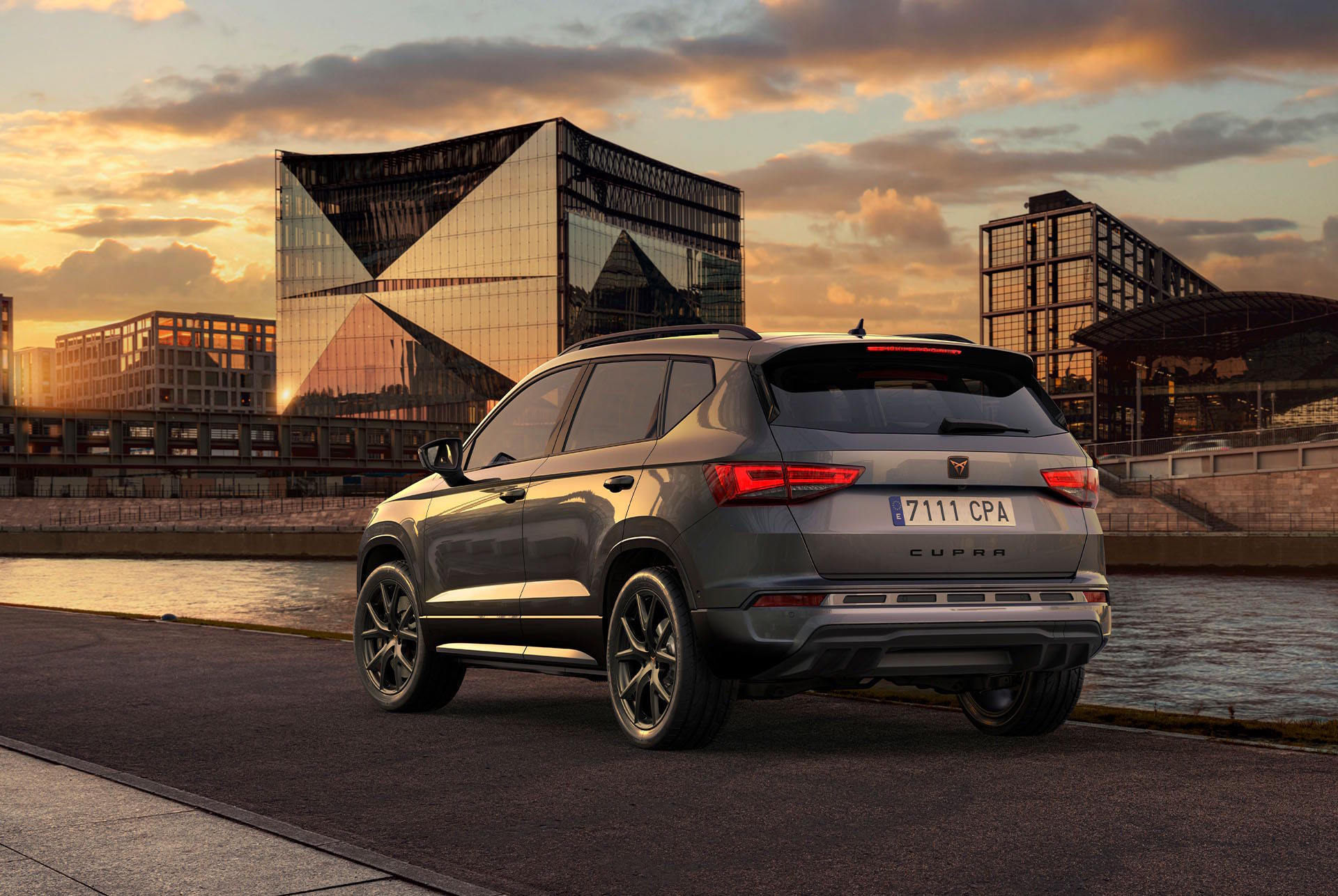 CUPRA Ateca parked beside a riverside walkway at sunset with modern buildings in the background.