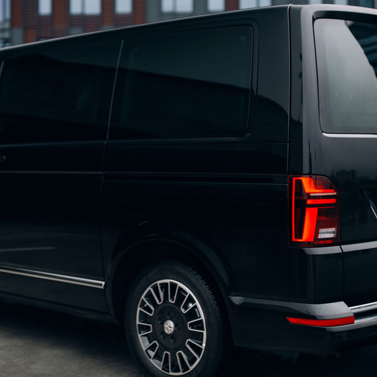Rear side view of a black Volkswagen van showing tail light and wheel.