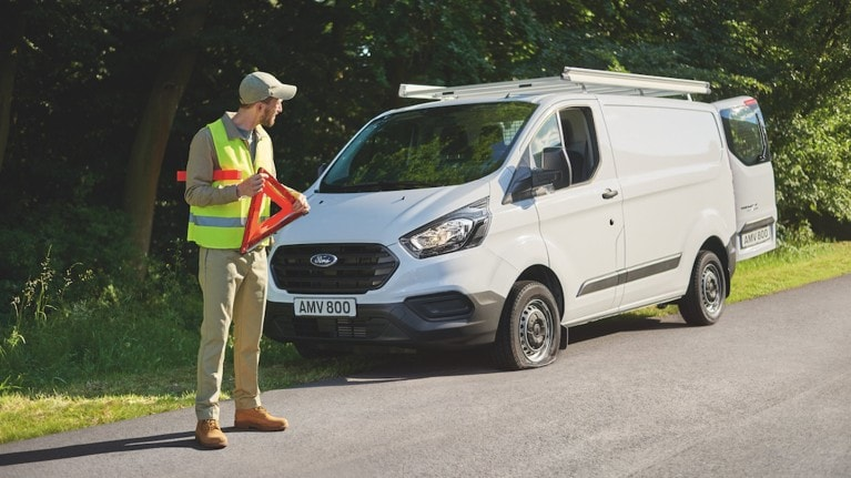 Person in a bright safety vest holding a hazard triangle with a Ford van in the background.