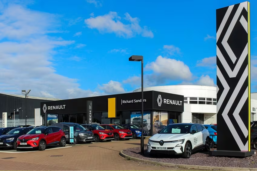 Wide exterior shot of Renault dealership forecourt with a range of Renault cars parked and showroom branding visible.