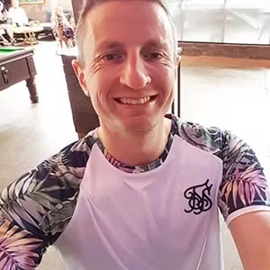 Person smiling for a casual selfie indoors while wearing a patterned short-sleeved top.
