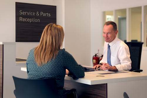 Customer speaking with a service advisor at the dealership reception desk.
