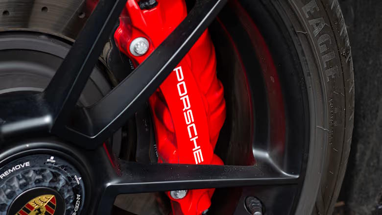 Close‑up of a Porsche alloy wheel showing a red brake caliper with white Porsche logo behind black wheel spokes.