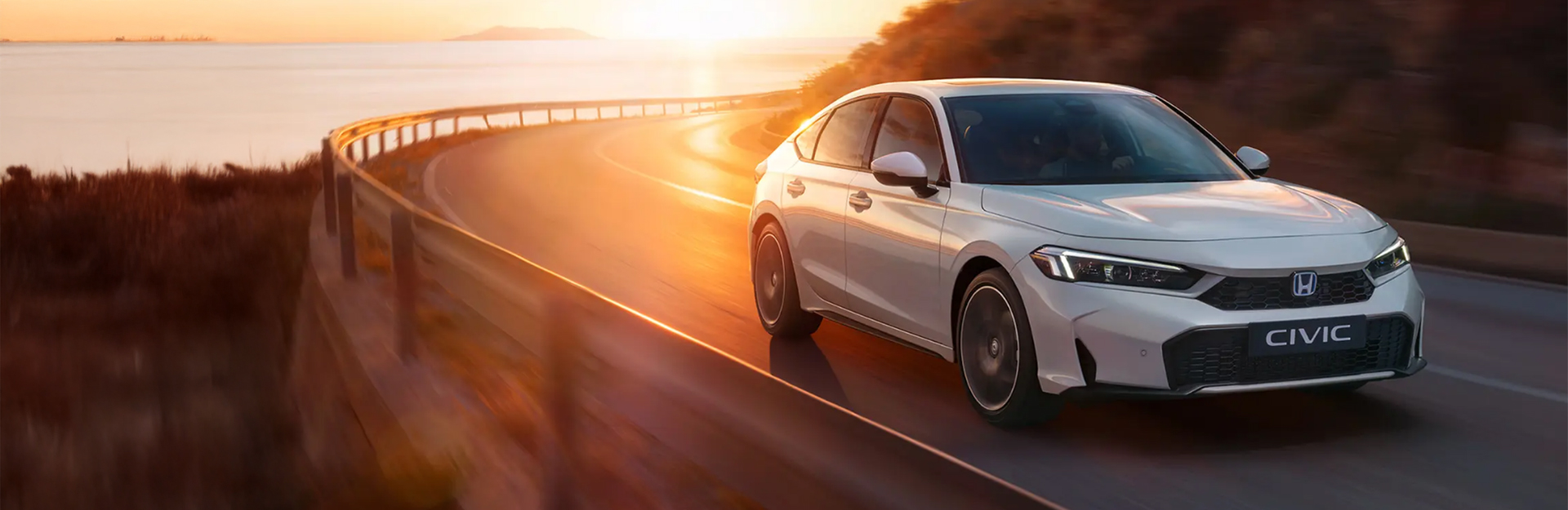 White honda civic driving on a mountain road at sunset.