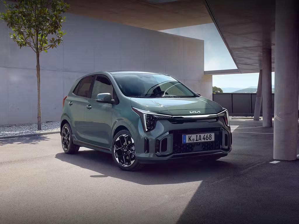 Front three-quarter view of the Kia Picanto in sage green, featuring distinctive boomerang-shaped LED daytime running lights, bold black alloy wheels and sporty front bumper design.