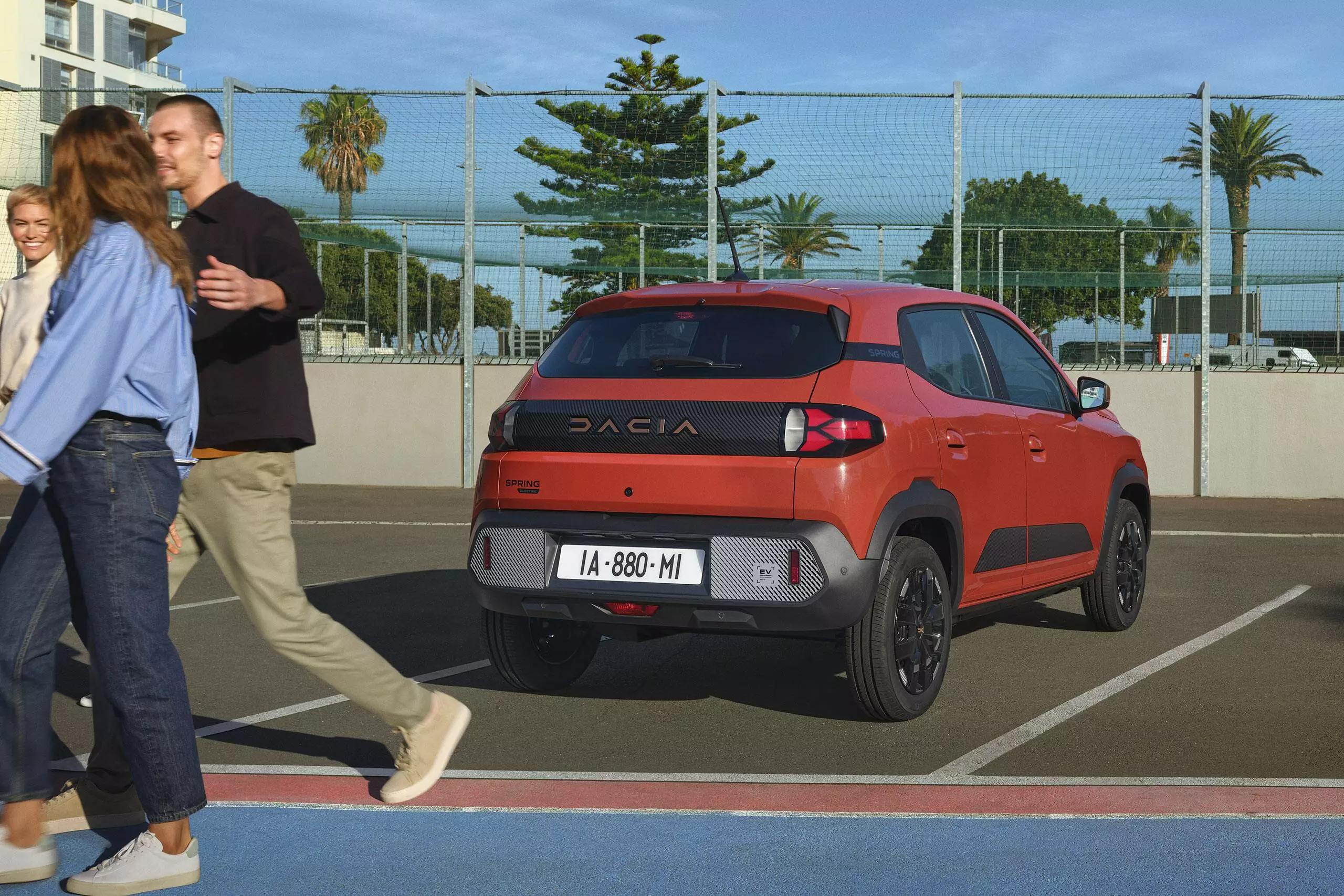 Dacia Spring parked in an outdoor sports court area as people walk past, showing everyday urban use.