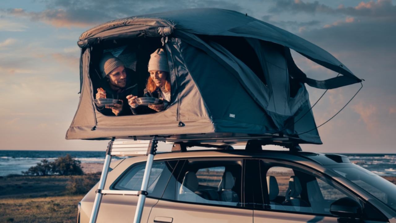 SUV fitted with rooftop tent overlooking seaside landscape.