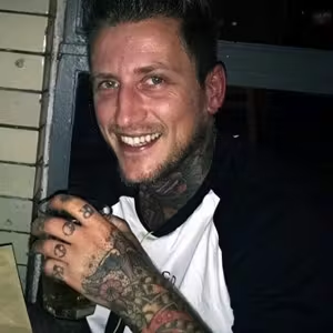 Person smiling while holding a drink during an evening social gathering.