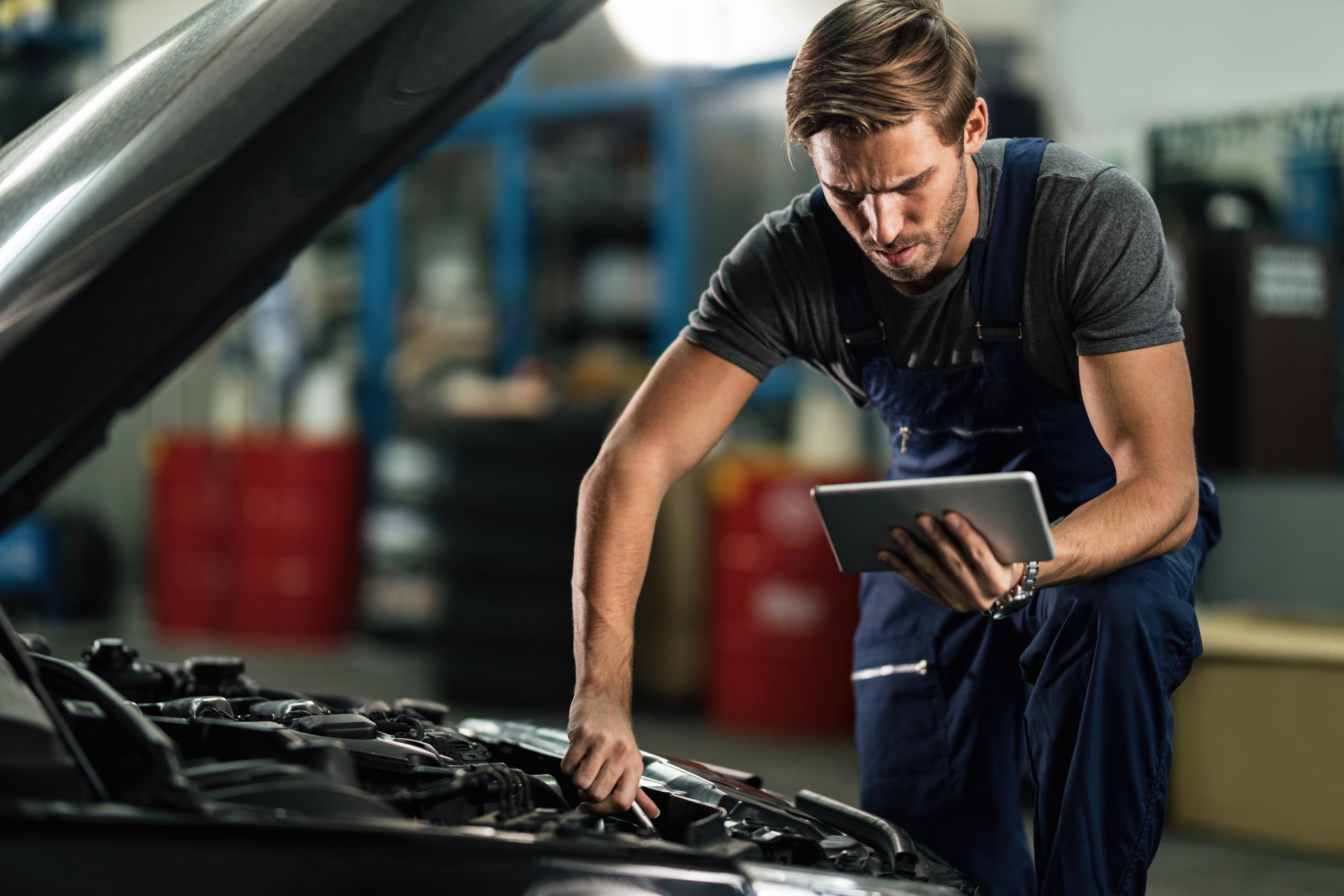 mechanic technician working at car engine with diagnostics