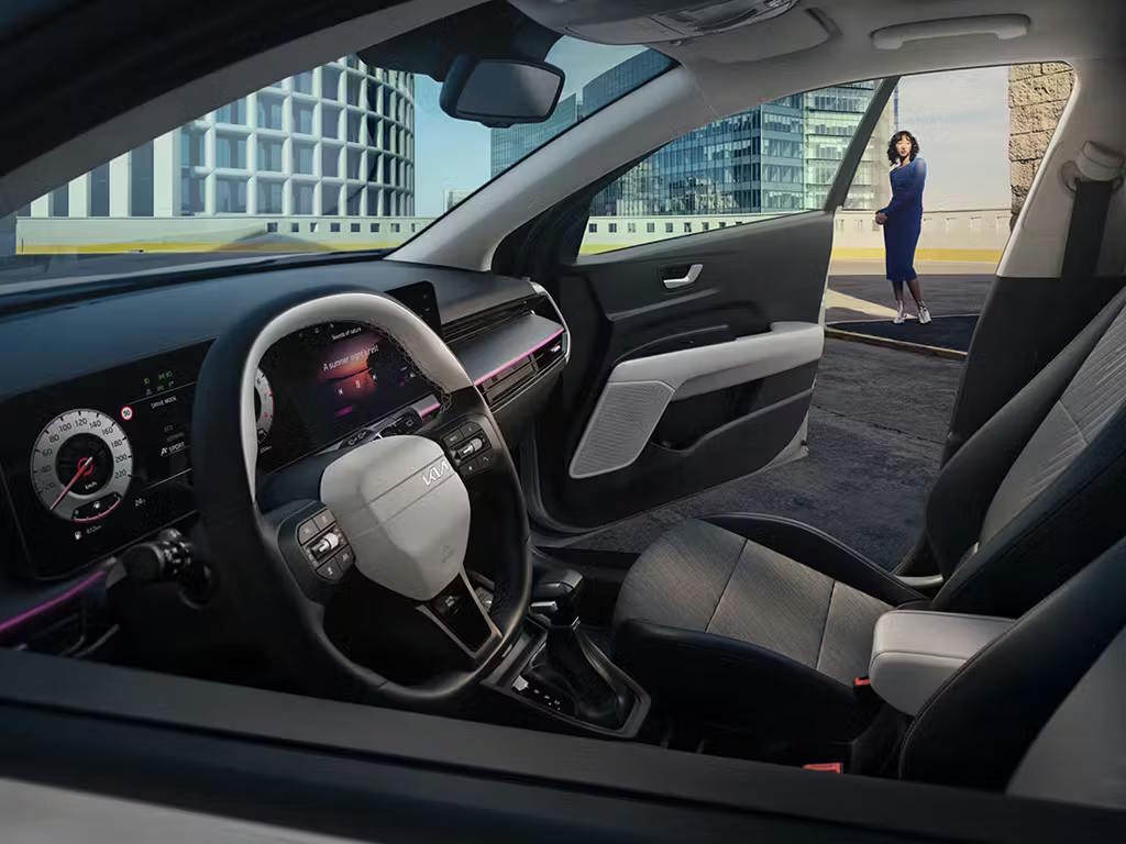 Interior view of the Kia Stonic from the driver's side, showcasing the two-tone steering wheel, digital instrument cluster, widescreen infotainment display and modern grey fabric upholstery.