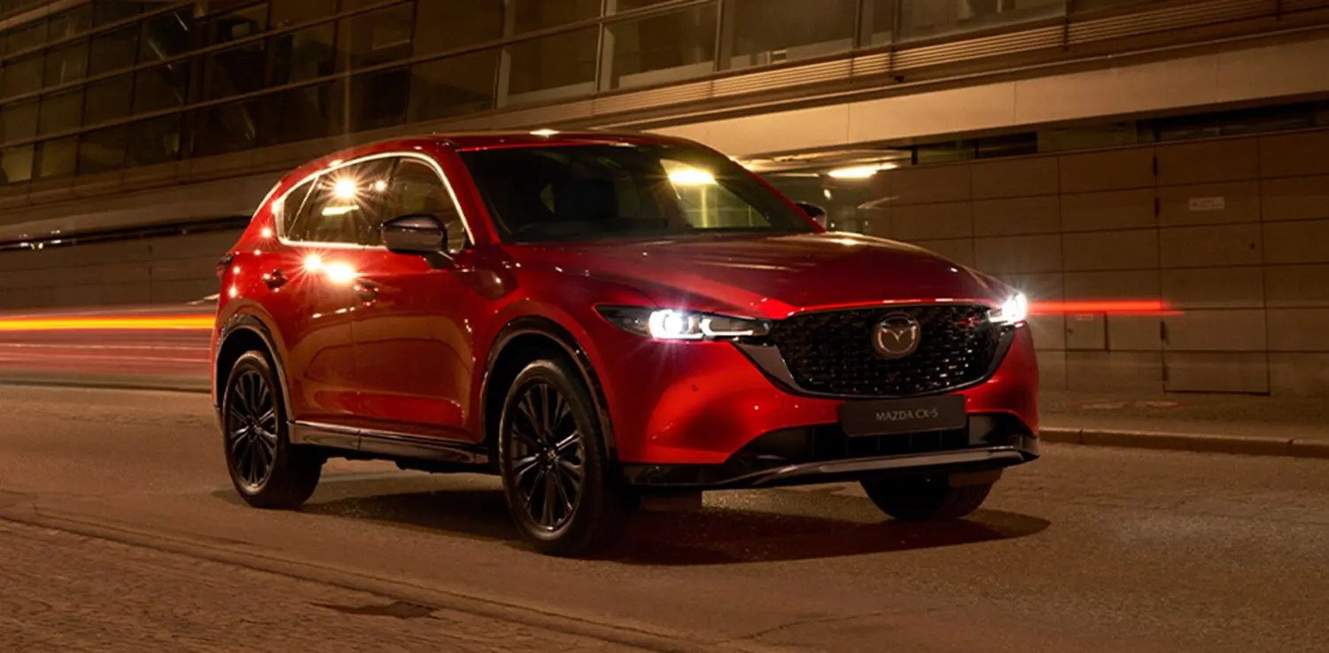 Mazda CX-5 Sport Black Edition in metallic red driving on an empty road in an urban night-time setting.