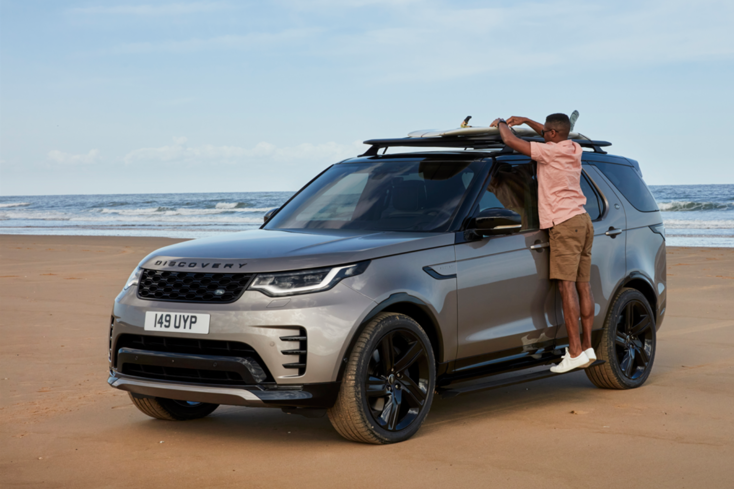 Land Rover Discovery parked on beach with surfboard on roof.