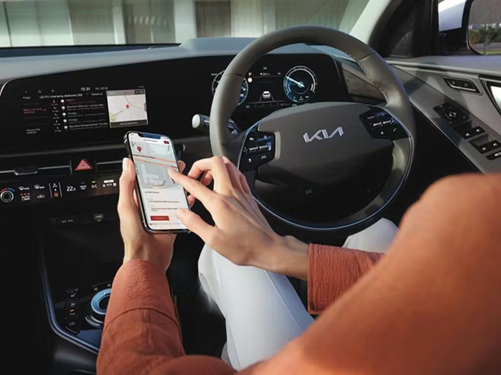 Driver using smartphone app inside the Kia Niro, showcasing the modern cockpit with curved dual-screen display, digital instrument cluster and flat-bottomed steering wheel.